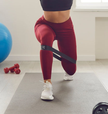 Kvinna tränar benmuskler med rött träningsband i hemmet